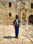 Primary view of [The Alamo historical site with reenactor wearing a face mask]