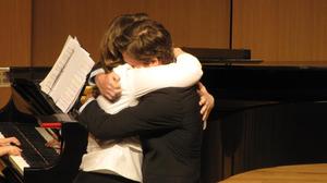 [Two singers hugging on stage at the Student recital during Jake Heggie's residency]