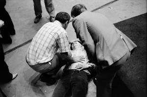 [Man lying on the ground with two men crouched over him]