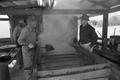 Photograph: [Hulen Wilcox and another man standing near the sugar cane evaporator]