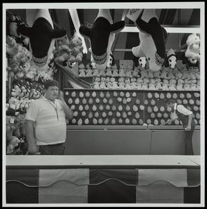[Two people working a balloon dart carnival game]