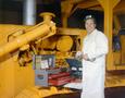 Photograph: [Man posing next to a large yellow machine with a open tool box]