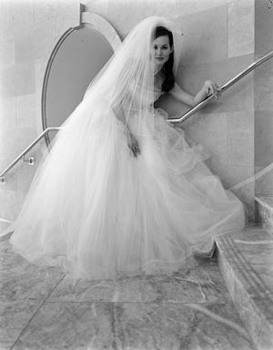 [A model posing in a wedding dress and veil on a marble staircase]