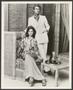 Photograph: [Woman seated in a chair and a man standing next to her.]