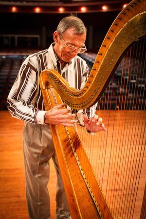 [David Williams looking down while playing a harp]