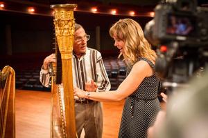 [Dr. Jaymee Haefner plucking a harp held by David Williams]