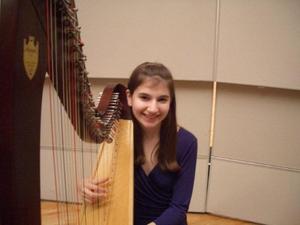 [A girl in a purple dress sitting behind a harp]