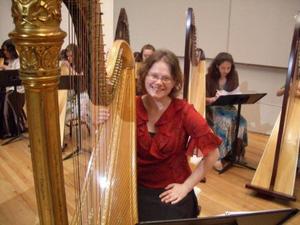 [A woman in a red shirt sitting behind a harp]