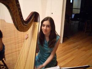 [A girl in a light blue dress sitting behind a harp]