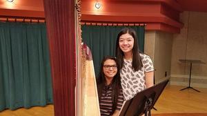 [Two girls posing next to a harp and a music stand]