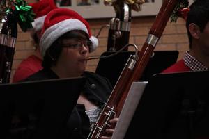 [A person playing a bassoon adorned with an ornament and tinsel]