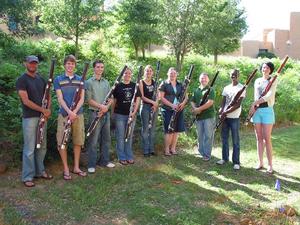 [Nine people holding bassoons while standing next to bushes]