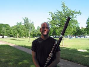 [A man in a dark t-shirt and glasses posing with a bassoon]
