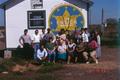 Photograph: [People posed in front of a house with a large round sign]