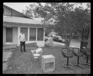 [Man standing in a front yard among furniture]