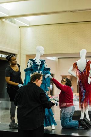 [Staff adjusting a mannequin sporting a blue silk dress]