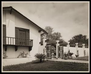 Primary view of object titled '[A stucco home with wood shingles and a gate]'.