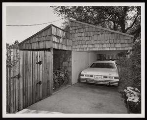 Primary view of object titled '[A car and bicycles parked under shingle-covered overhangs]'.