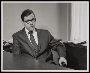 [A man in a suit sitting behind a desk]