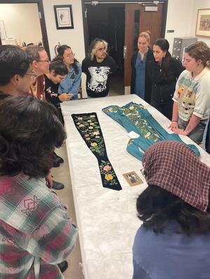 [Students examining an 1888 tea dress and a painted velvet panel]