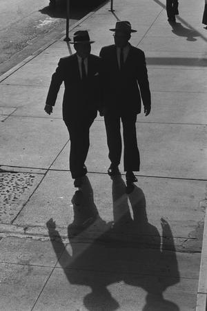 [Two silhouetted men on a sidewalk]