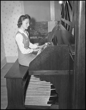 [Woman seated at and playing the organ]