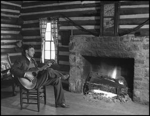[Young man playing guitar by the fireplace]
