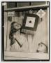 Photograph: [Photograph of a young girl hanging a banner from a window frame]