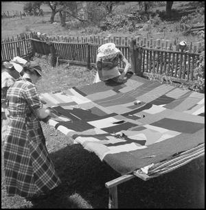 [Photograph of three women hand sewing a quilt together]