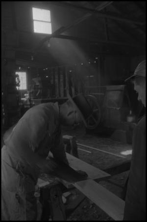 [Photograph of a man sawing a board into two]