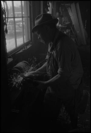 [Photograph of a man grinding the head of a pickaxe]