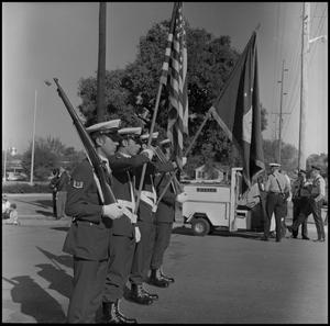 [Uniformed flag-bearers in a line, one holding a rifle]