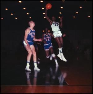 [NTSU basketball player in mid air, one hand on the ball]