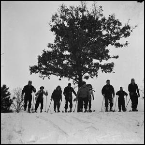 [Nine skiers standing at the top of a hill]