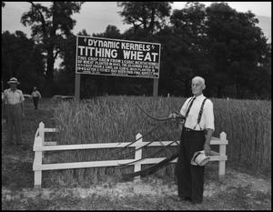 [Man standing in front of a small plot of wheat, holding a scythe]