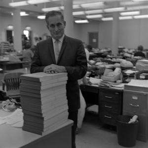 [John L. Carter standing next to a stack of books]