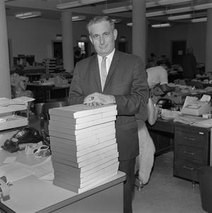 [John L. Carter standing next to a stack of books, 3]