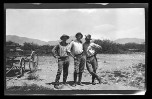 [Three men standing and posing in a desert]