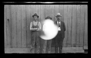 Primary view of object titled '[Photo of three men standing in front of a fence]'.