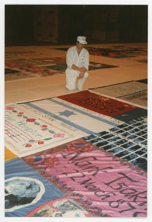 [Man in White Kneels Beside AIDS Memorial Quilt Section]