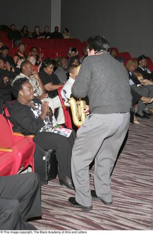 [Man playing a saxophone for audience members]