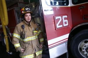 [A fireman stands beside fire engine #26, wearing his fire-fighting gear]