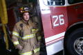 Primary view of [A fireman stands beside fire engine #26, wearing his fire-fighting gear]