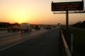 Photograph: [Vehicles pass an Amber Alert sign beside the highway at sunset]