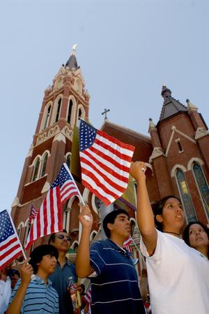 [Protesters march and wave American flags as they pass Cathedral Santuario de Guadalupe in Dallas]
