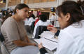 Primary view of [A woman listens to another woman in a white coat in what appears to be a medical consultation]