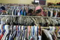Photograph: [Three people stand among racks of clothing in Dallas charity]